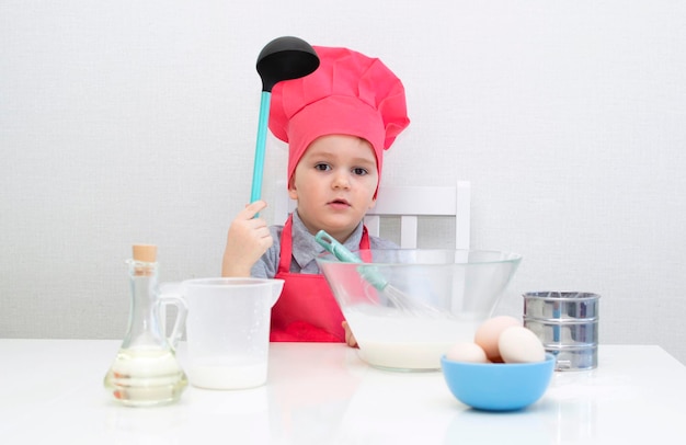 Cute little boy in a red chef hat kneads the pastry dough in a bowl. Homemade cakes.