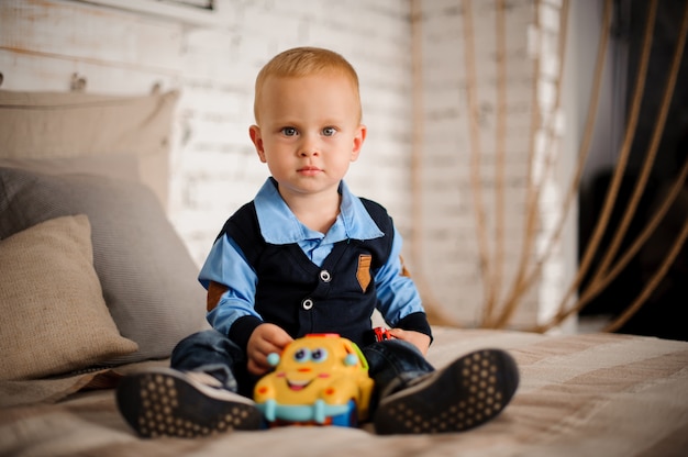 Cute little boy sitting on the bed with a toy in his hands