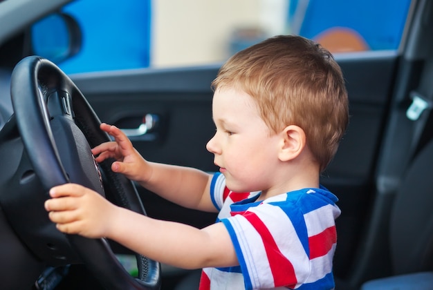 Foto simpatico ragazzino seduto in macchina e tiene il volante