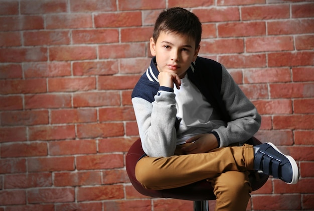 Cute little boy sitting on a chair near brick wall