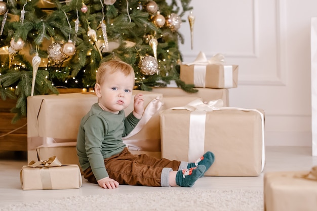 Cute little boy sitting under Christmas tree with gift box.