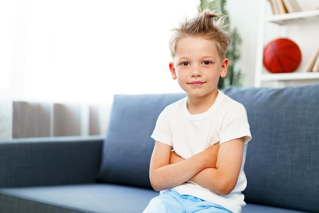 Cute little boy sitting on couch at home, looking at camera