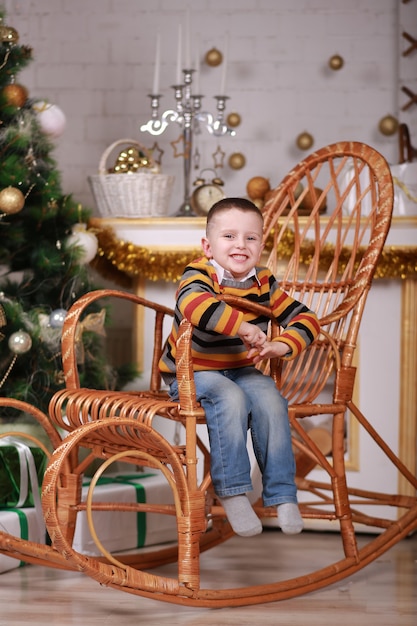 クリスマスツリーの近くのロッキングチェアに座っているかわいい男の子。