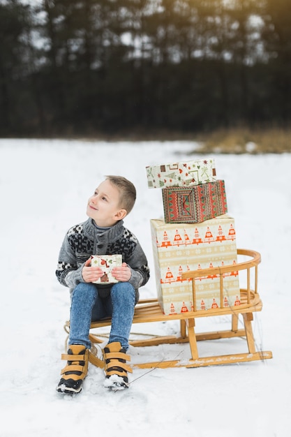 Cute little boy, sitting on a wooden sledge decorated with presents boxes