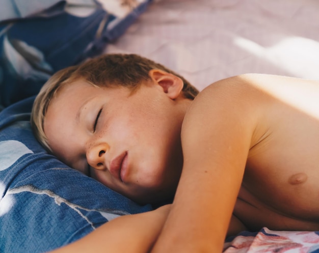 Photo cute little boy sleep sweetly on pillow with bright morning sunbeams from window taking a nap happy bedtime for kids problem of early awakening late falling asleep health sleep biorhythms