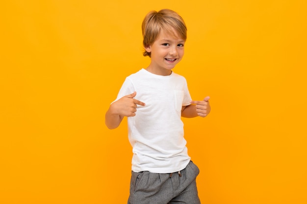 Cute little boy in t-shirt and trousers smiles and shows himself isolated on yellow