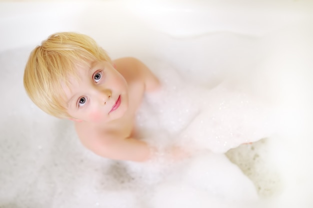 Cute little boy taking a foam bubble bath view from above