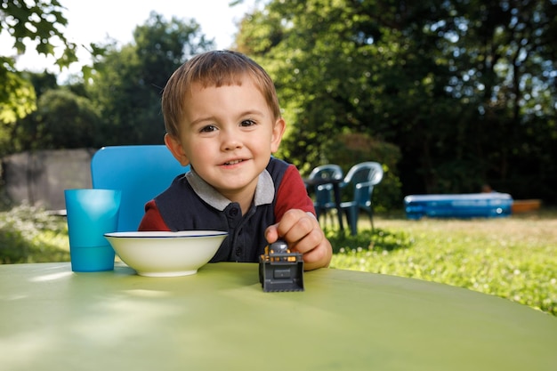 A cute little boy of three years is eating cornflakes outside