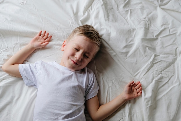 Cute little boy toddler sleeping lying on a white bed in the morning