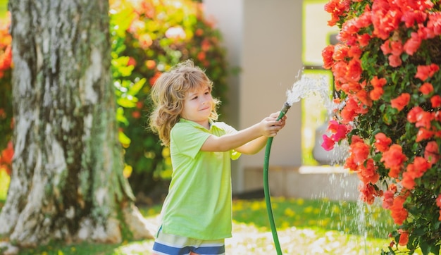 Cute little boy watering flowers in the garden at summer day Child using garden hose Funny kid watering plants in the yard garden