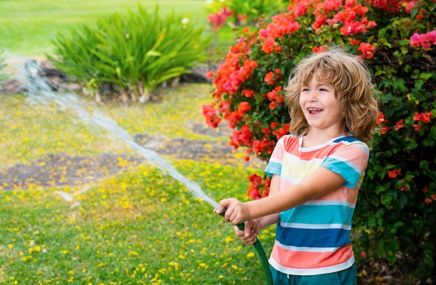 Cute little boy watering flowers in the garden at summer day child using garden hose funny kid