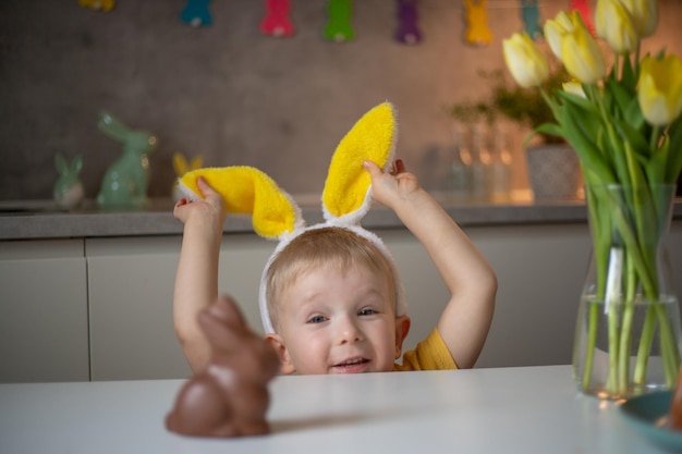 イースターの日にうさぎの耳をかぶったかわいい男の子は、チョコレートのイースターバニーを食べたがっています イースターのためにエッグハントをする子供 自宅でイースターを祝うチャーミングな子供