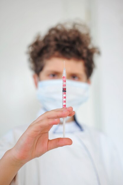 Photo cute little boy wears a medical uniform and a mask holds a syringe playing doctor