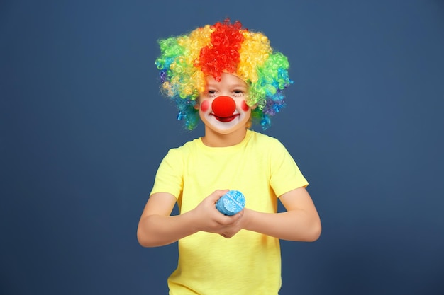 Cute little boy with clown makeup and party popper on color background April fool's day celebration