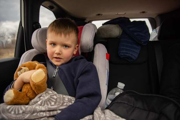 Cute little boy with fluffy bear in car chair at back seats in road trip