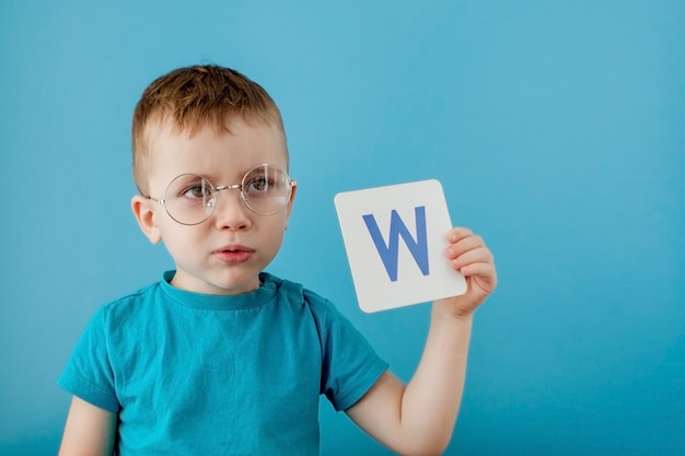 Cute little boy with letter on blue wall. Child learning a letters. Alphabet