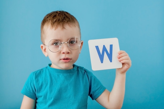 Cute little boy with letter on blue wall. Child learning a letters. Alphabet