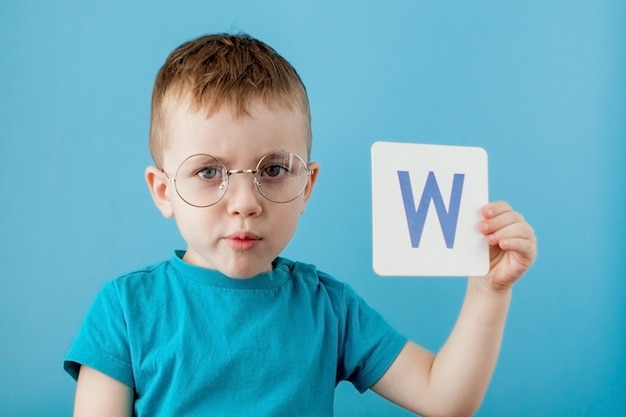 Милый маленький мальчик с письмом на голубой стене. ребенок учится буквы. алфавит