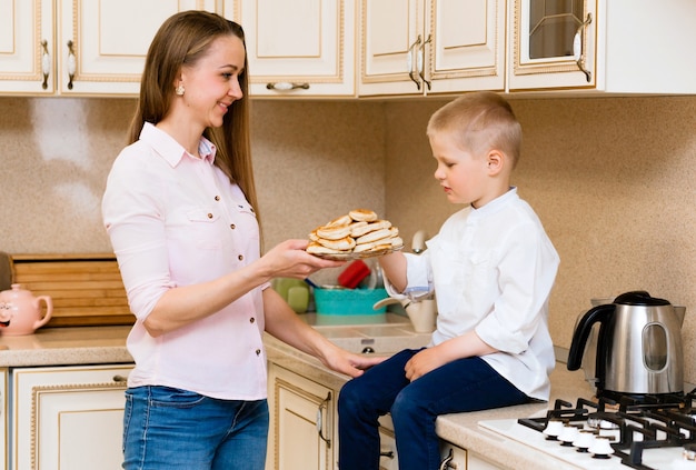 Ragazzino sveglio con la madre. famiglia in cucina. madre con figlio che mangia frittelle. cottura fatta in casa