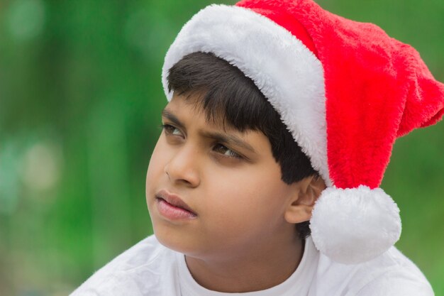 A cute little boy with Santa cap looking sideways at a distance 