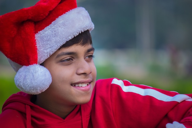 산타 모자 빨간 티셔츠를 입은 귀여운 소년이 행복하게 웃고 멀리 바라보고 있습니다