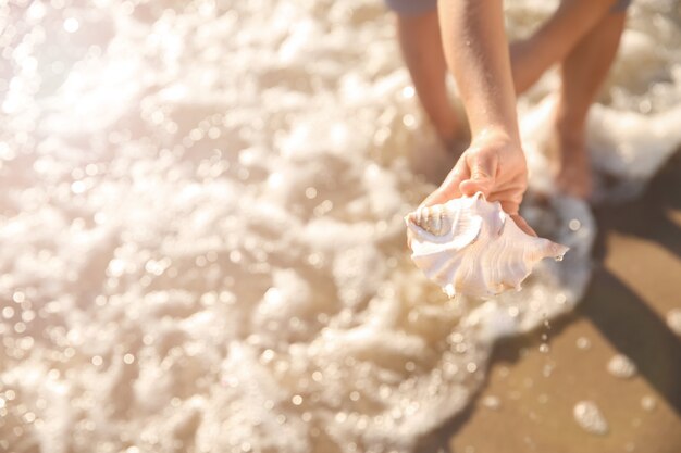 Ragazzino carino con conchiglia sulla spiaggia