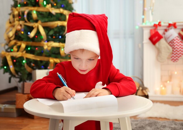 Cute little boy writing letter to Santa Claus at table