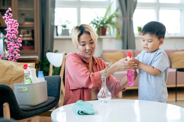 ダスターに消毒剤をスプレーするかわいい男の子と若いアジアの女性