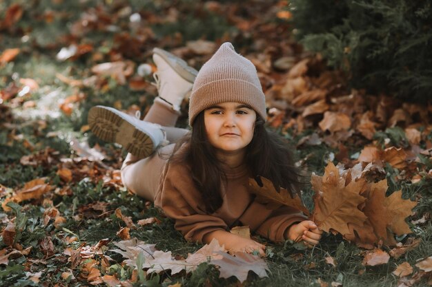 Cute little brunette girl lying on the grass in autumn