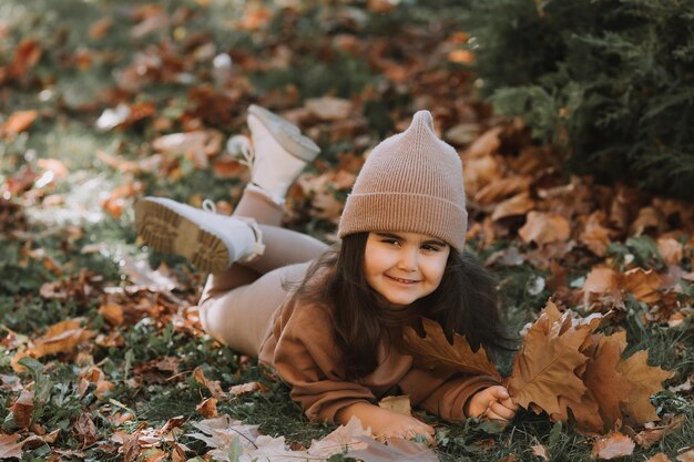 Cute little brunette girl lying on the grass in autumn