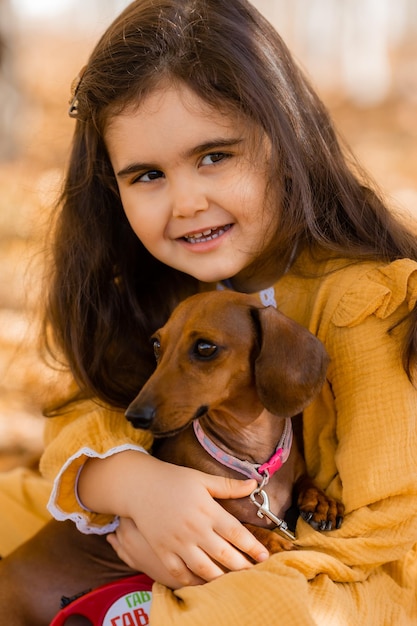 Cute little brunette girl walks in autumn with a dachshund dog in the park