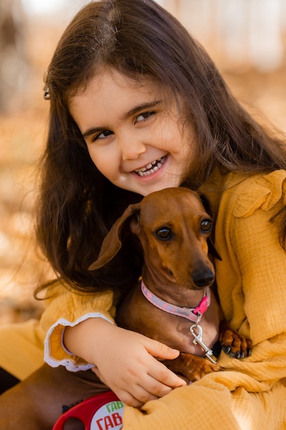 Cute little brunette girl walks in autumn with a dachshund dog in the park