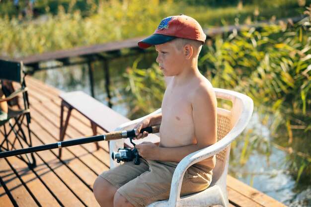 CUTE LITTLE CAUCASIAN BOY SITTING ON PIER FISHING using fishing pole