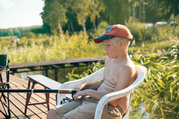 CUTE LITTLE CAUCASIAN BOY SITTING ON PIER FISHING using fishing pole