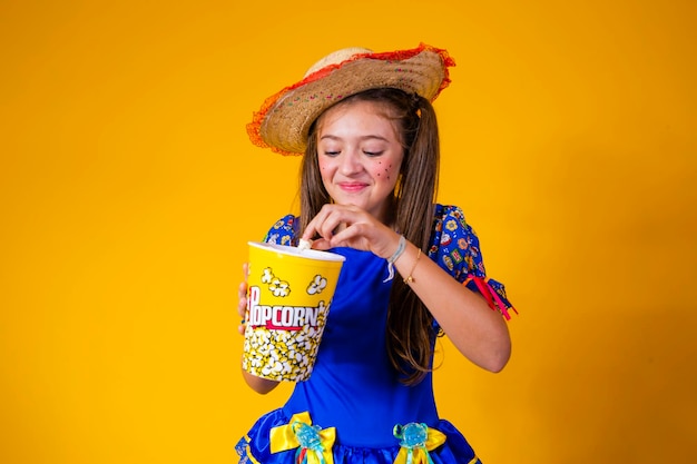 Piccola ragazza caucasica sveglia nel tipico vestito da festa junina che mangia popcorn