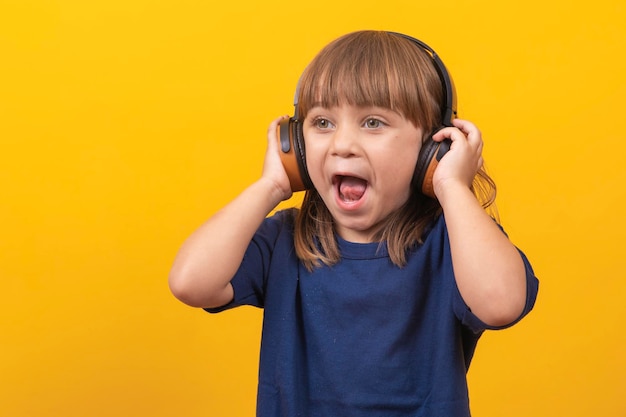 黄色の背景で音楽を聴くヘッドフォンでかわいい白人少女