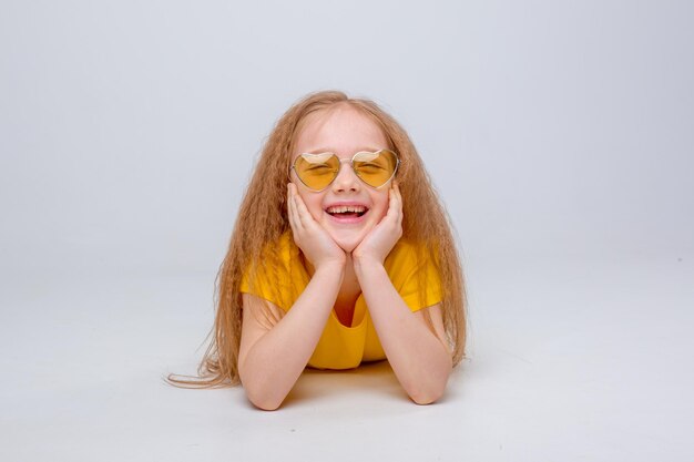 Cute little cheerful girl in sunglasses in a yellow Tshirt on a white background