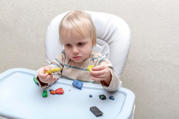 家で遊んでいるかわいい小さな男の子が色とりどりのプラスチックを成形している子供たちの手が色付きの粘土スタッコで彫刻