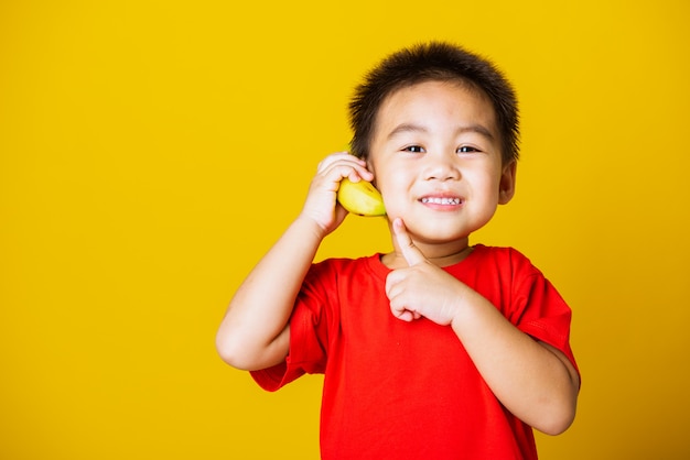 かわいい小さな子供男の子の笑顔が電話のようにふりをしてバナナの果実を保持しています。