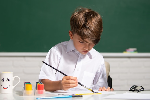 教室で描くかわいい小さな子供学校でアートとクラフトのレッスンを楽しんでいる男子生徒の肖像