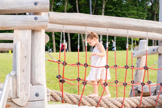 cute little child girl in dress playing on kids playground in summer day