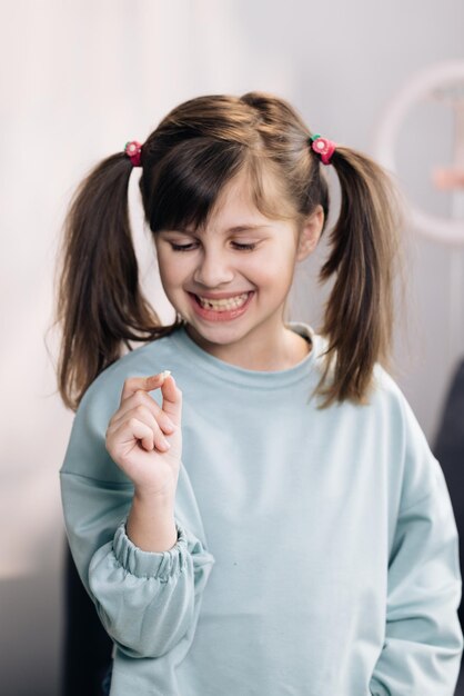 Cute little child girl is rejoices and showing her lost milk tooth and smiling to camera