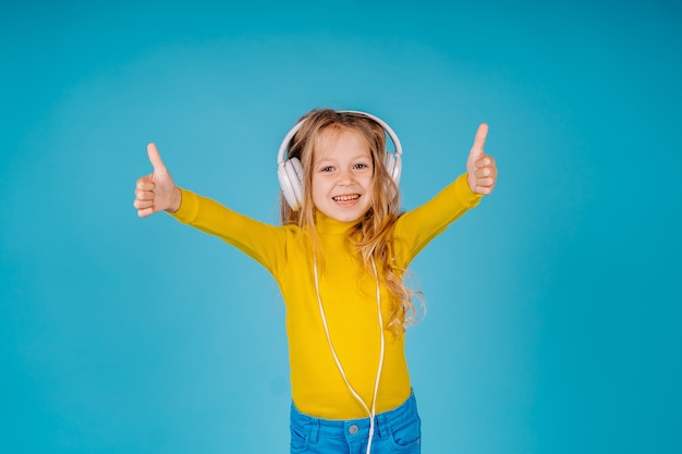 Cute little child girl listen to music on big headphones isolated and shows okay gesture