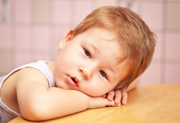 Cute little child laid his head on his hands at the table