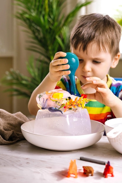 A cute little child pours warm water over toys frozen in ice dinosaur defrosting early development