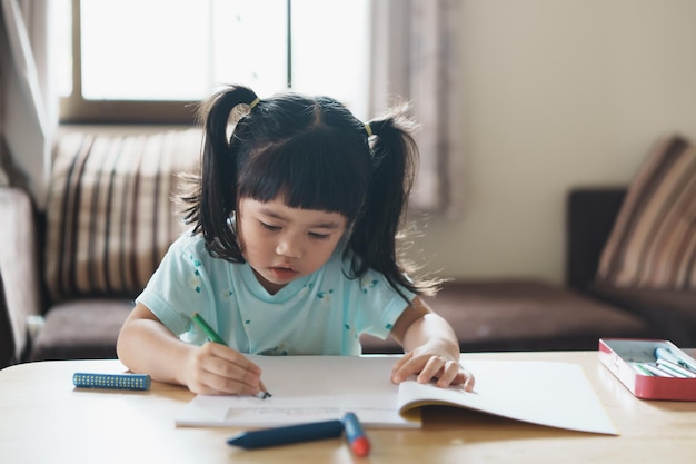 Милый маленький ребенок в розовой рубашке держит карандаш или делает домашнее задание или рисует цвет дерева красочными красками