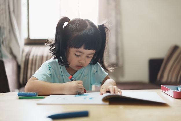 ピンクのシャツを着たかわいい子供が鉛筆を持ったり、宿題をしたり、カラフルな絵の具で木色の絵を描いたり、木の色を使って色を描いたりするアジアの女の子赤ちゃんのアーティストの活動ライフスタイルのコンセプト