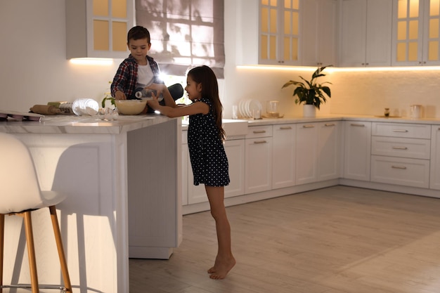 Cute little children cooking dough in kitchen at home