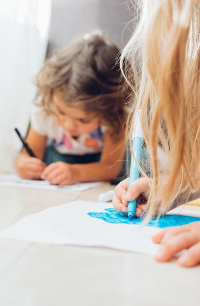 Foto piccole bambine carine che giacciono sul pavimento e disegnano con i marcatori a colori