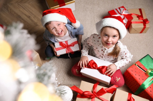 Cute little children with Christmas gifts on floor at home above view